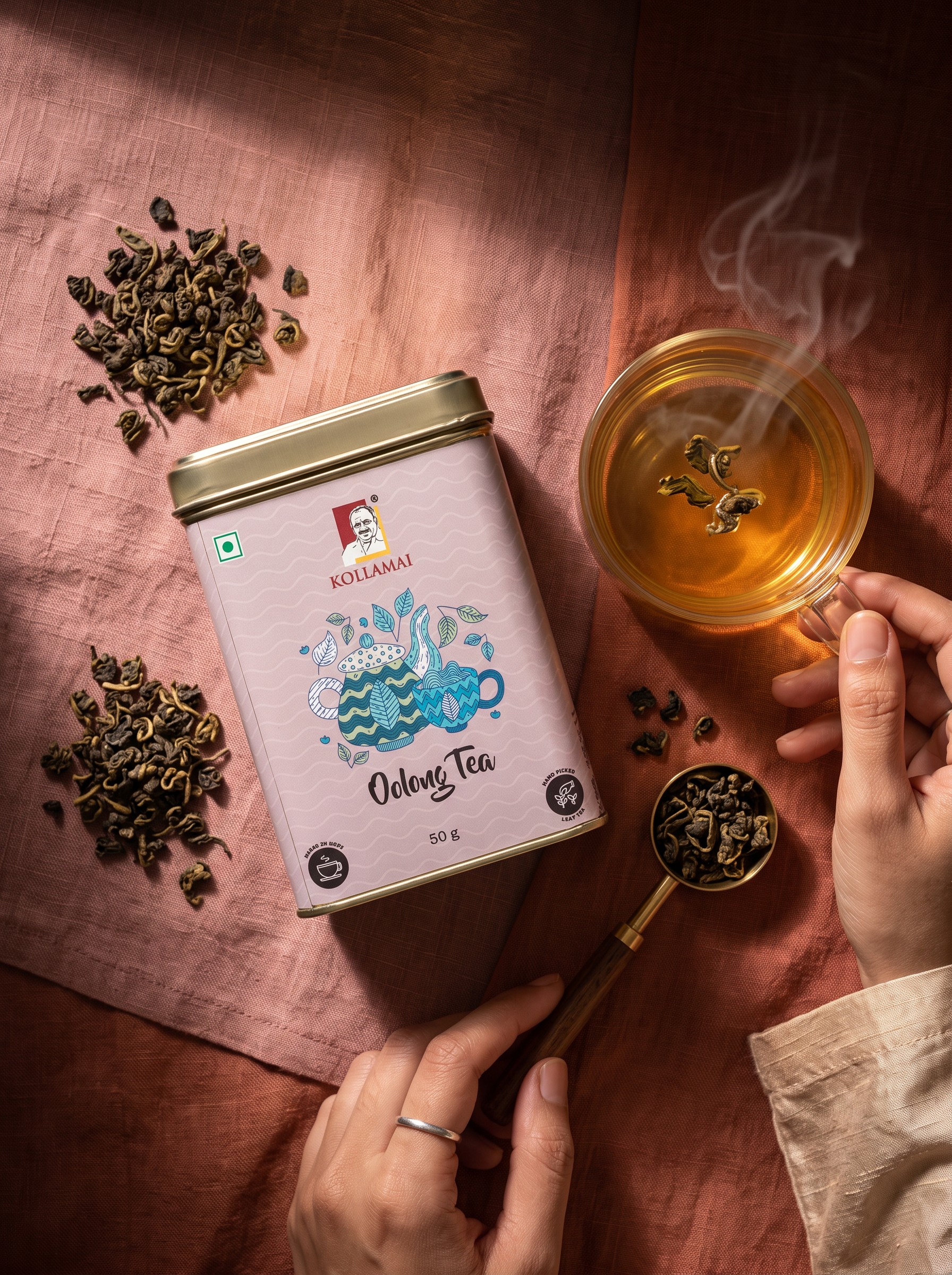 Kollamai Oolong Tea – Premium Loose Leaf Flat Lay Kollamai Oolong Tea tin with a cup of golden oolong tea and loose tea leaves on a dusty rose linen surface