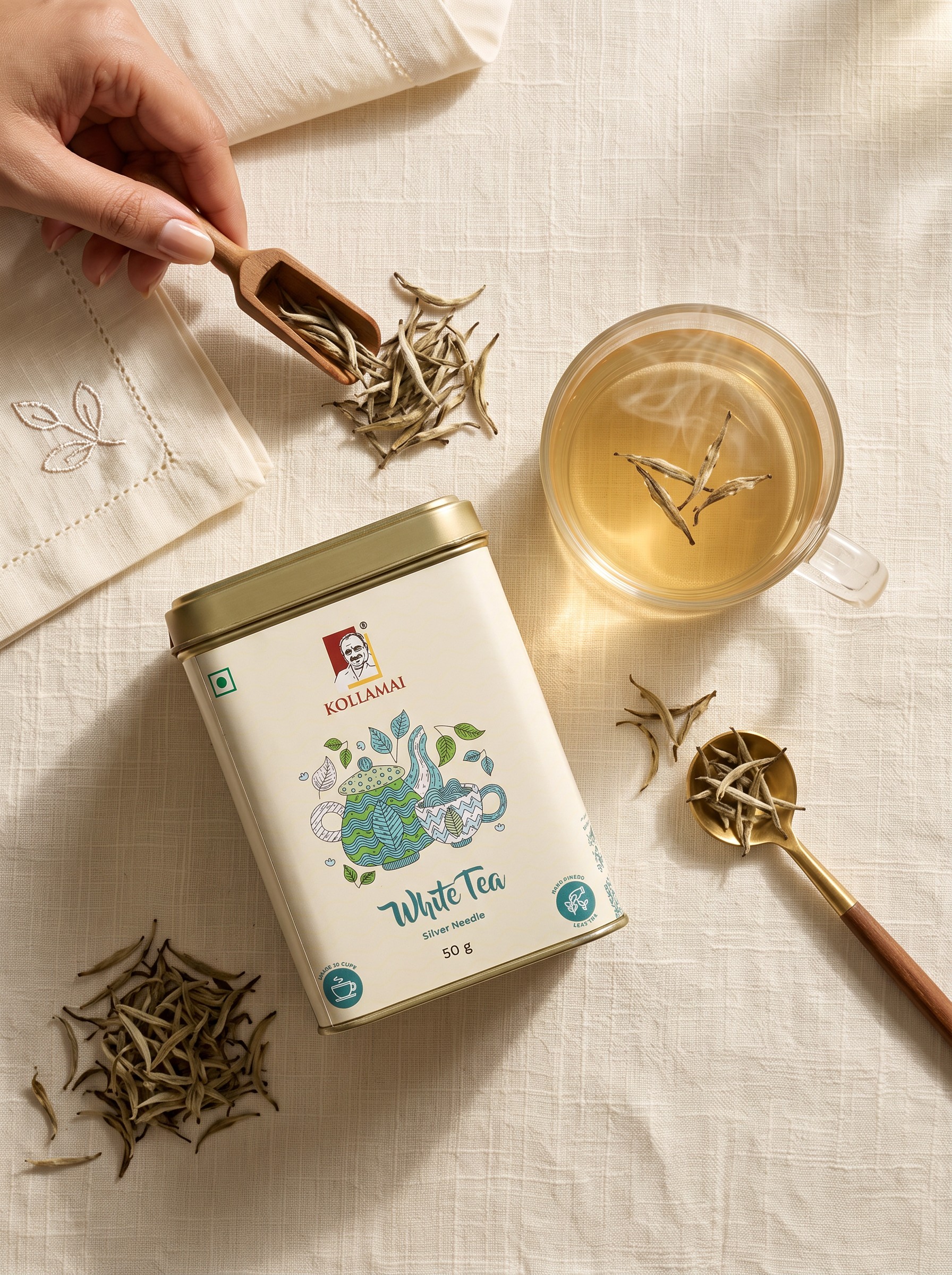 Kollamai White Tea – Premium Loose Leaf Flat Lay Kollamai White Tea tin with a cup of pale white tea and loose tea buds on a cream linen surface