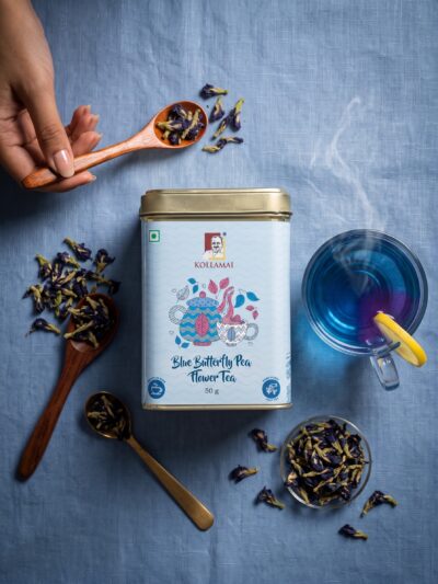 Kollamai Blue Butterfly Pea Flower Tea tin with a cup of vivid blue tea and dried flowers on a soft blue linen surface