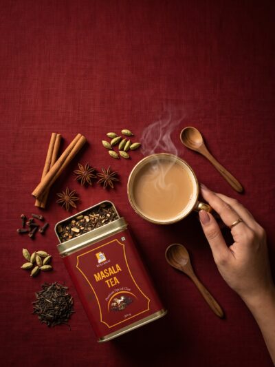 Kollamai Masala Tea tin with whole spices and steaming cup of spiced chai